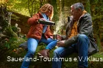 A couple take a coffee break on a tree trunk in the forest.